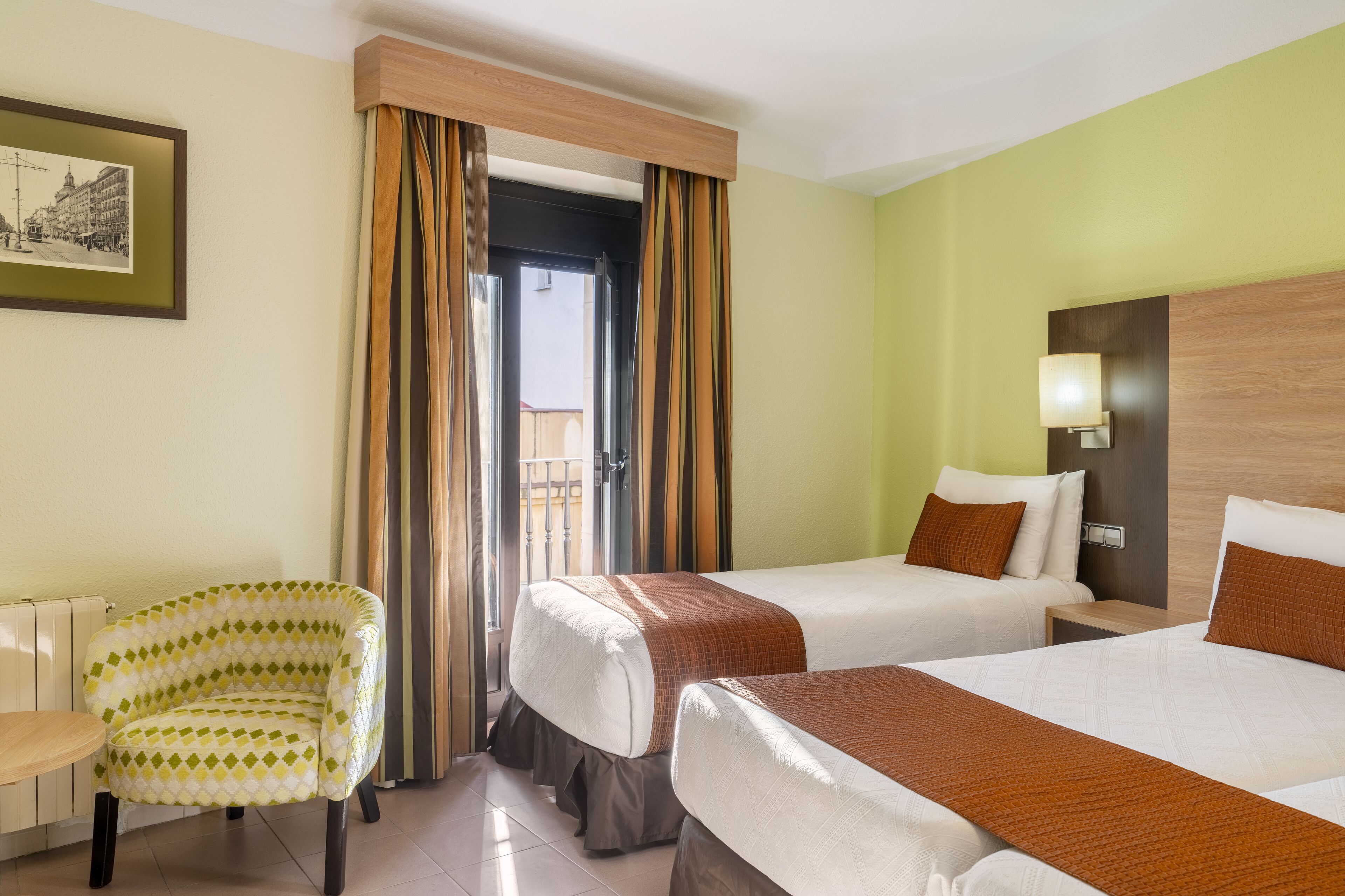 A hotel room with two beds, a chair, a table, and a framed picture on the wall.