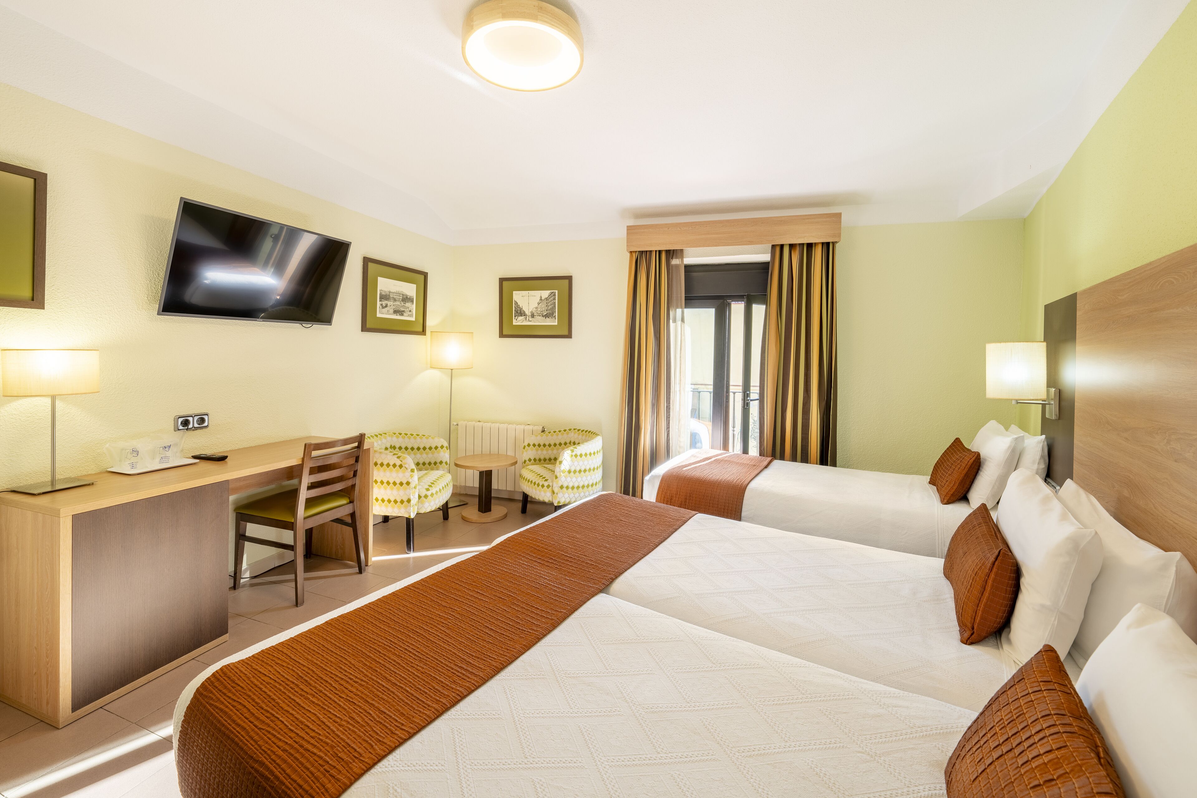 A hotel room with two beds, a desk, a chair, a TV, and a window with curtains.
