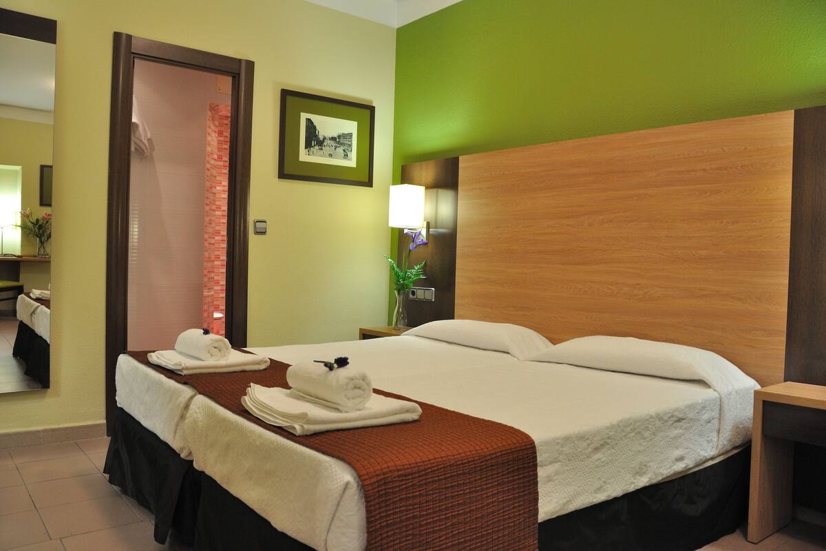 A hotel room with a double bed, a wooden headboard, a nightstand with a lamp, and a framed picture on the wall.