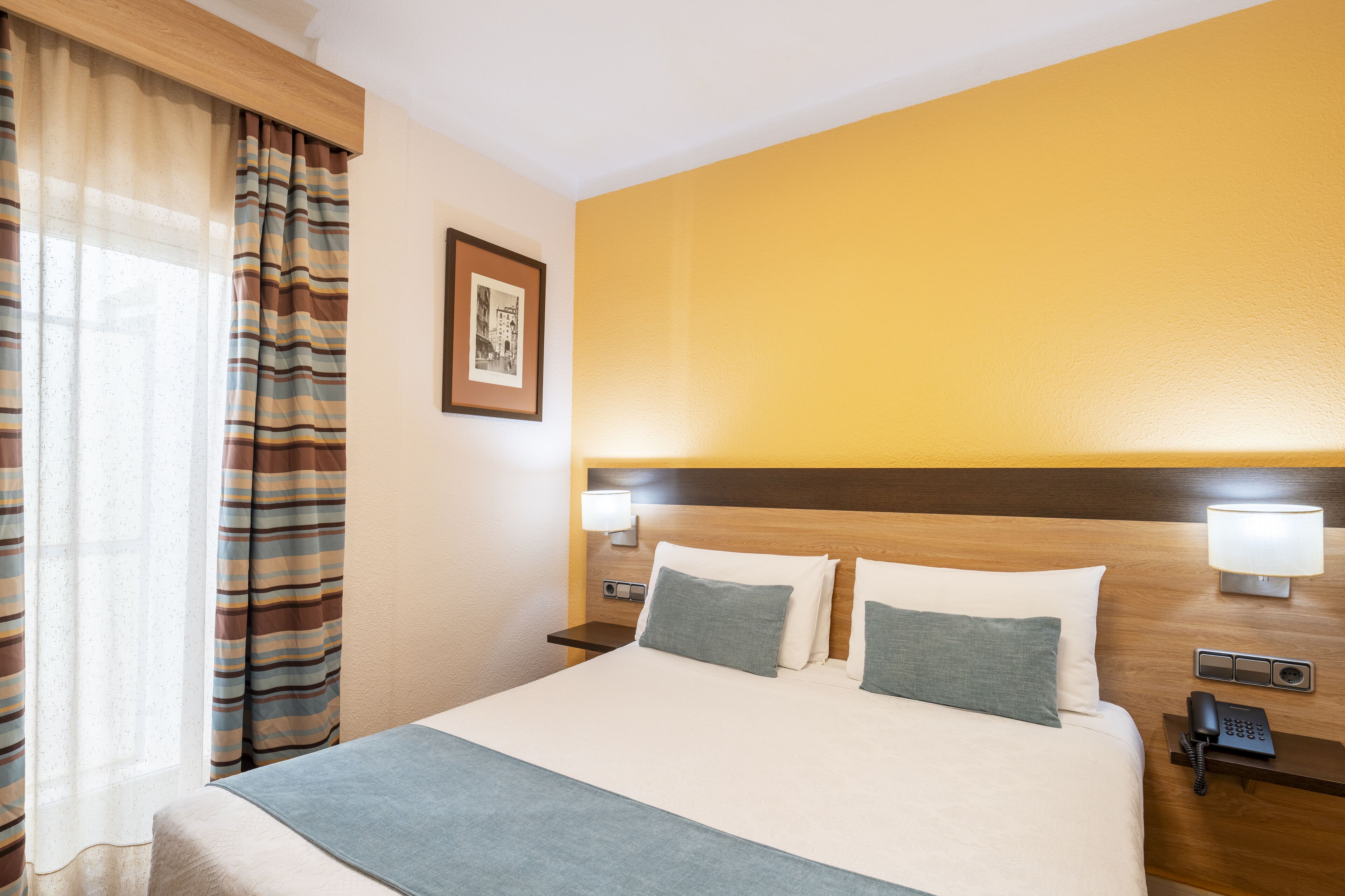 A hotel room with a large bed, two bedside lamps, a nightstand with a phone, and a framed picture on the wall.