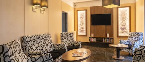 A modern lobby with patterned sofas, a round table, and a flat-screen TV on the wall.
