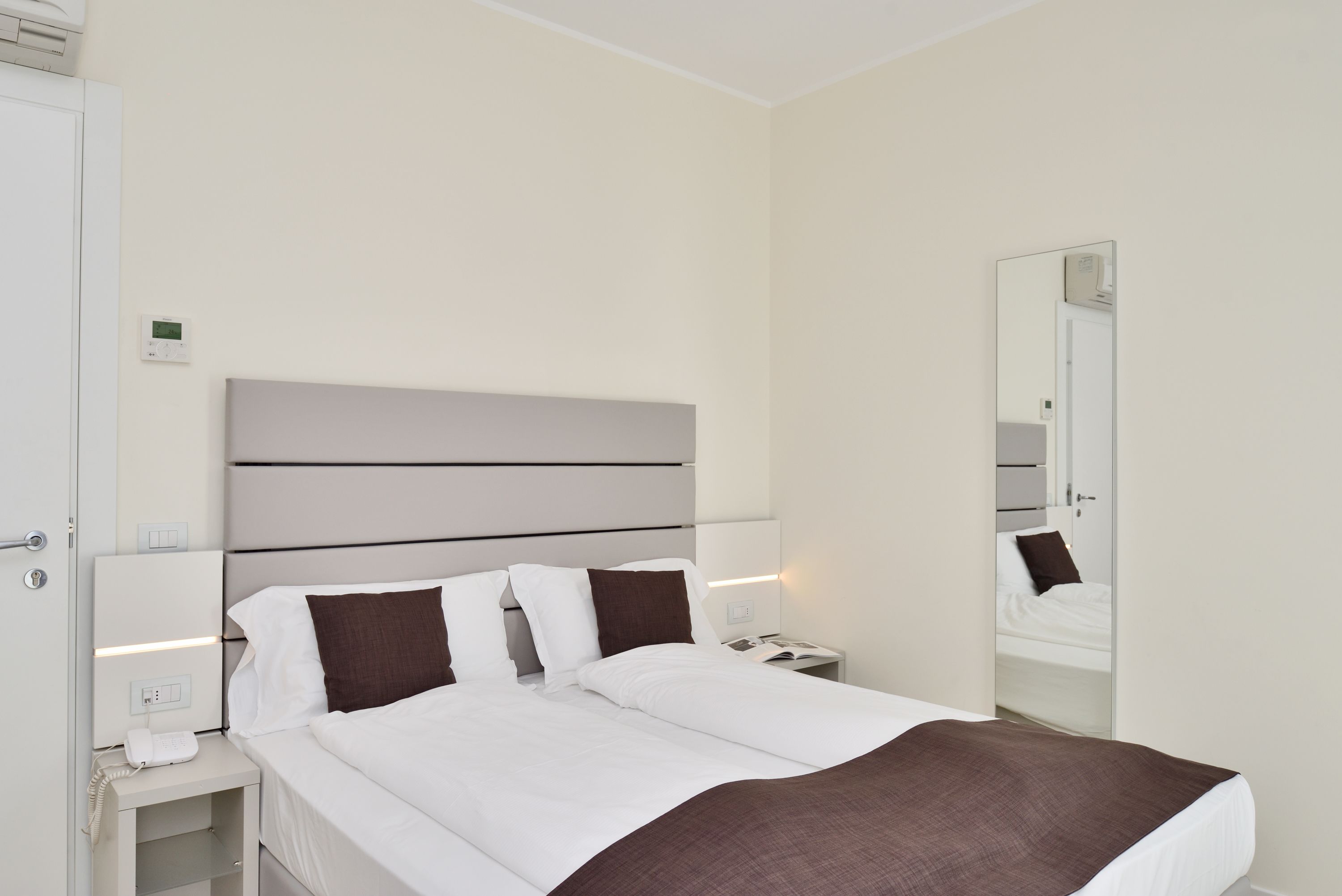 Een moderne hotelkamer met een groot bed, nachtkastjes, een spiegel en een wandthermostaat.