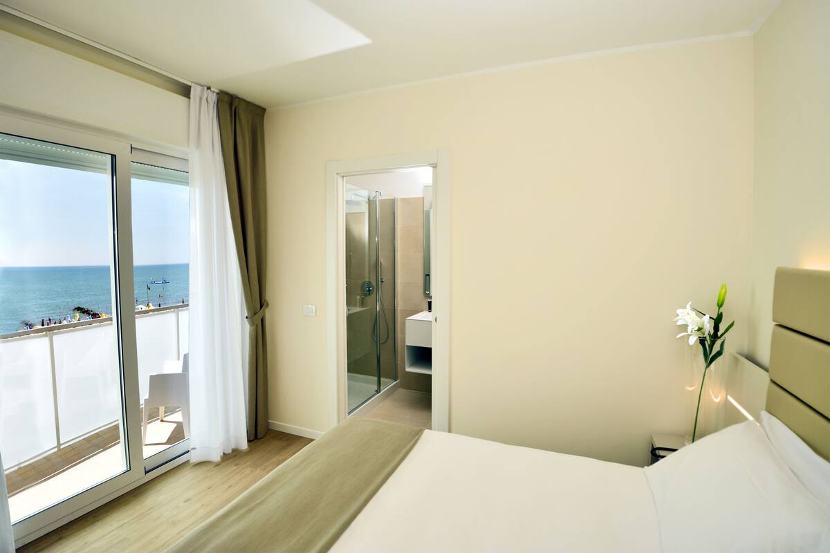 Habitación de hotel con cama, baño y balcón con vista al mar.