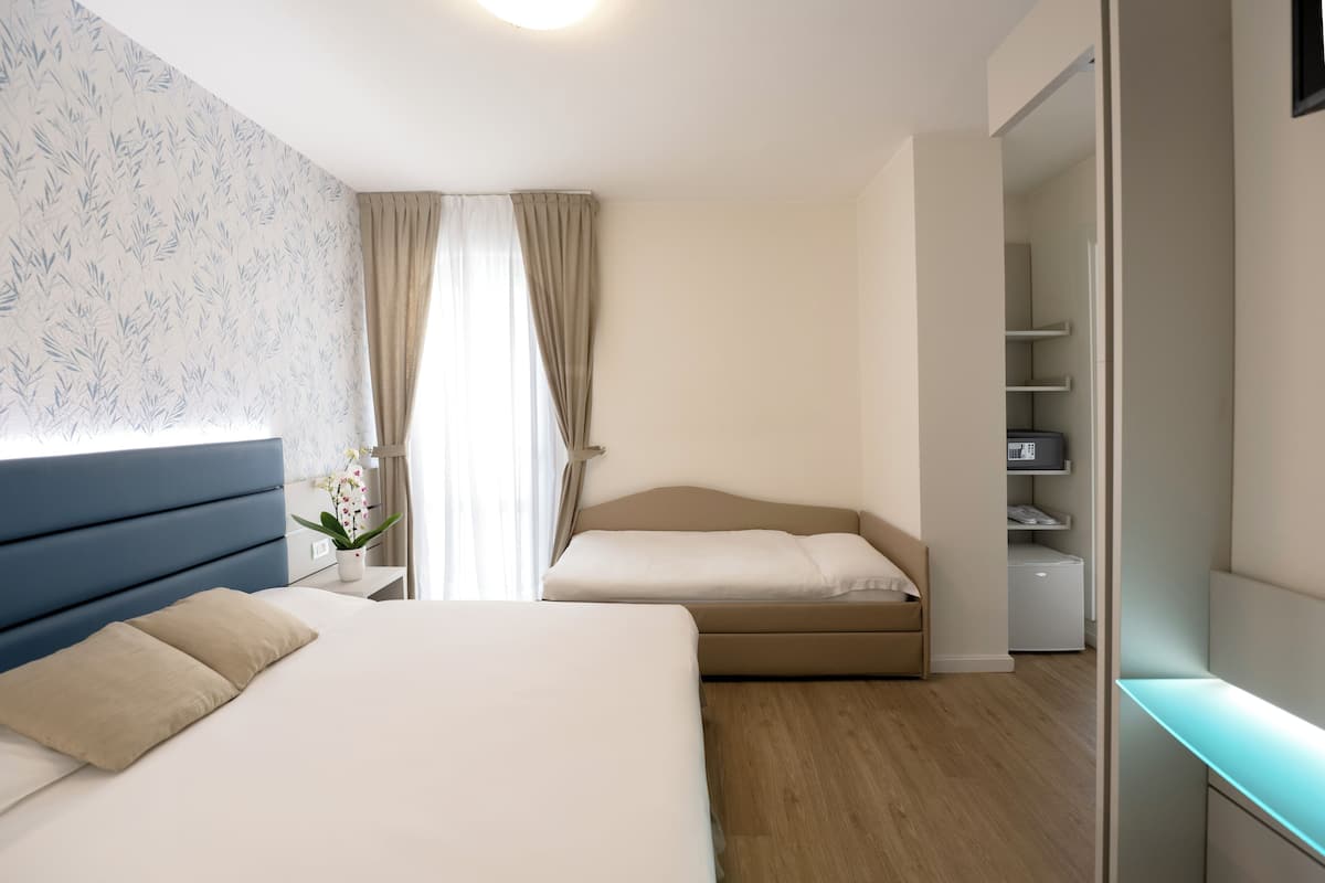 Un dormitorio moderno con una cama grande, un sofá cama más pequeño, un armario y un escritorio con lámpara.