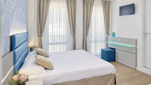 Un dormitorio moderno con cama, cortinas, televisor y mesita de noche.