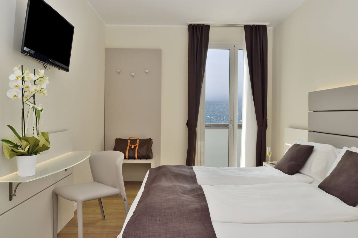 Habitación de hotel moderna con cama, escritorio, silla, televisor y vista al mar.