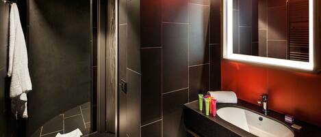 A modern bathroom with a curved shower, dark tiles, a large mirror, and a vanity with toiletries.