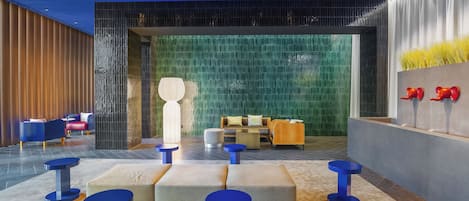 A modern lobby with a seating area featuring blue stools and cushioned benches, a reception desk, and a decorative wall with red objects.
