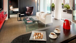 A modern hotel room with a glass coffee table, a red coffee maker, two cups of coffee, and a plate of pastries. - Hotel Glam Milano (Milan)