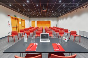 A conference room with a long table, red chairs, a laptop, and water bottles.