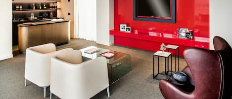 A modern living room with a red accent wall, a flat-screen TV, a bar area with shelves, and two white armchairs.