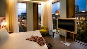 A hotel room with a large bed, a TV, a small table, and a view of a cityscape. - Hotel Glam Milano (Milan)