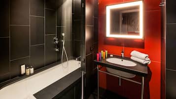 Une salle de bain moderne aux couleurs noir et rouge, comprenant une baignoire, une douche, un lavabo avec un miroir et des articles de toilette.