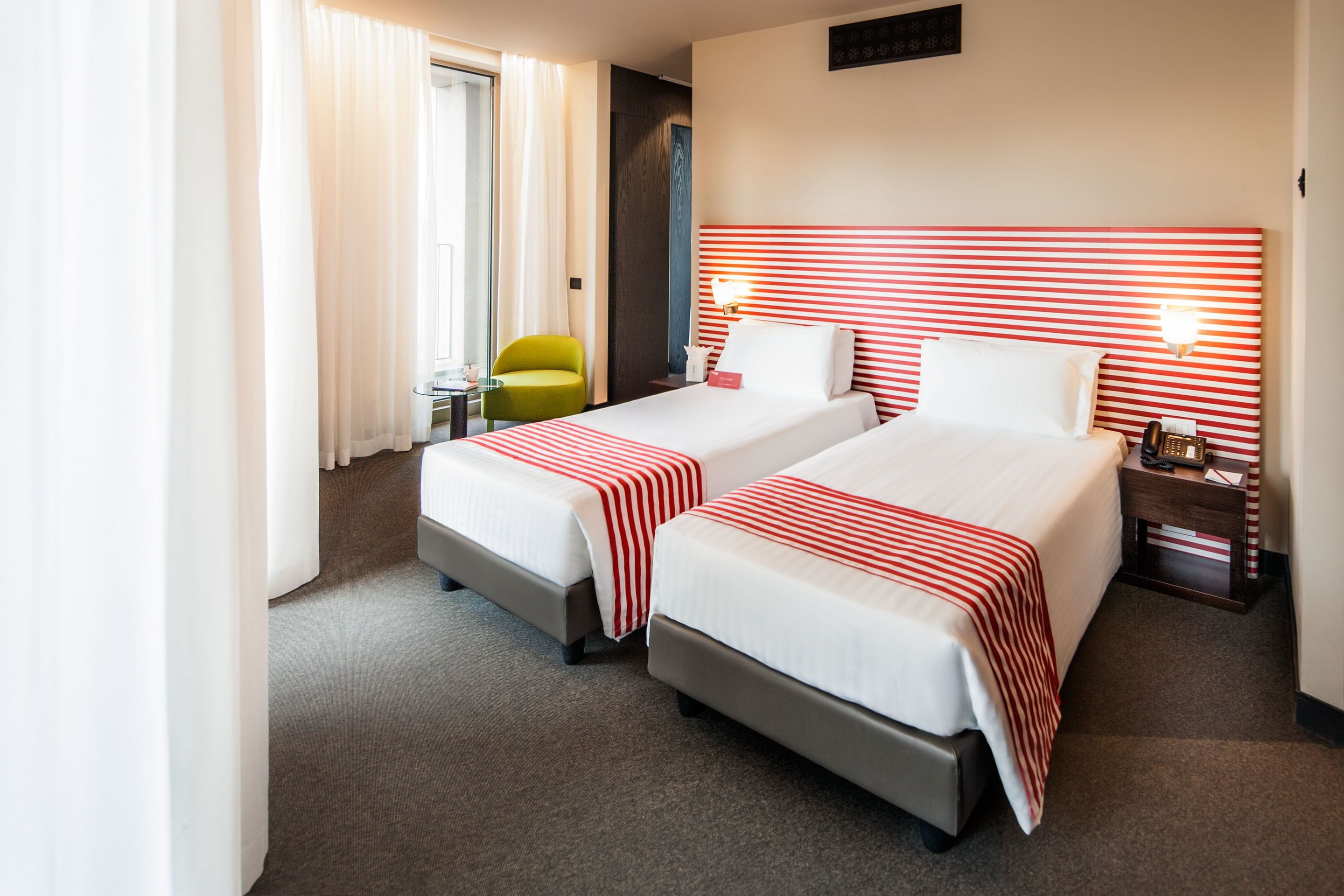 A hotel room with two beds, a small table, a chair, and a nightstand with a phone.