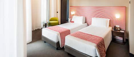 A hotel room with two beds, a small table, a chair, and a nightstand with a phone.