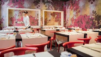 Ein Restaurant mit gedeckten Tischen, einem Kellner, der Gäste bedient, und floraler Wandgestaltung.