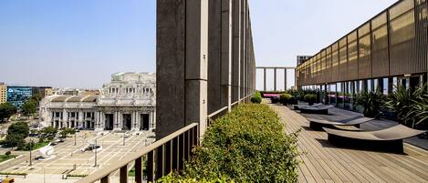 A modern building with a rooftop terrace featuring seating areas and a view of a historic building in the background.
