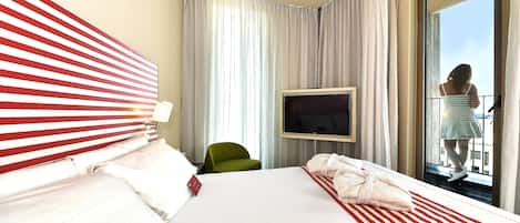 Une chambre d’hôtel avec un grand lit, un téléviseur fixé au mur, un fauteuil vert et un balcon avec vue.