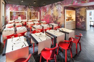 Un restaurant avec des chaises et des tables rouges, une femme à l’arrière-plan et un motif floral sur le mur.