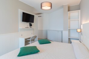 A bedroom with a bed, two green pillows, a desk, a chair, a television, and a wardrobe. - Hotel Austria (Caorle)