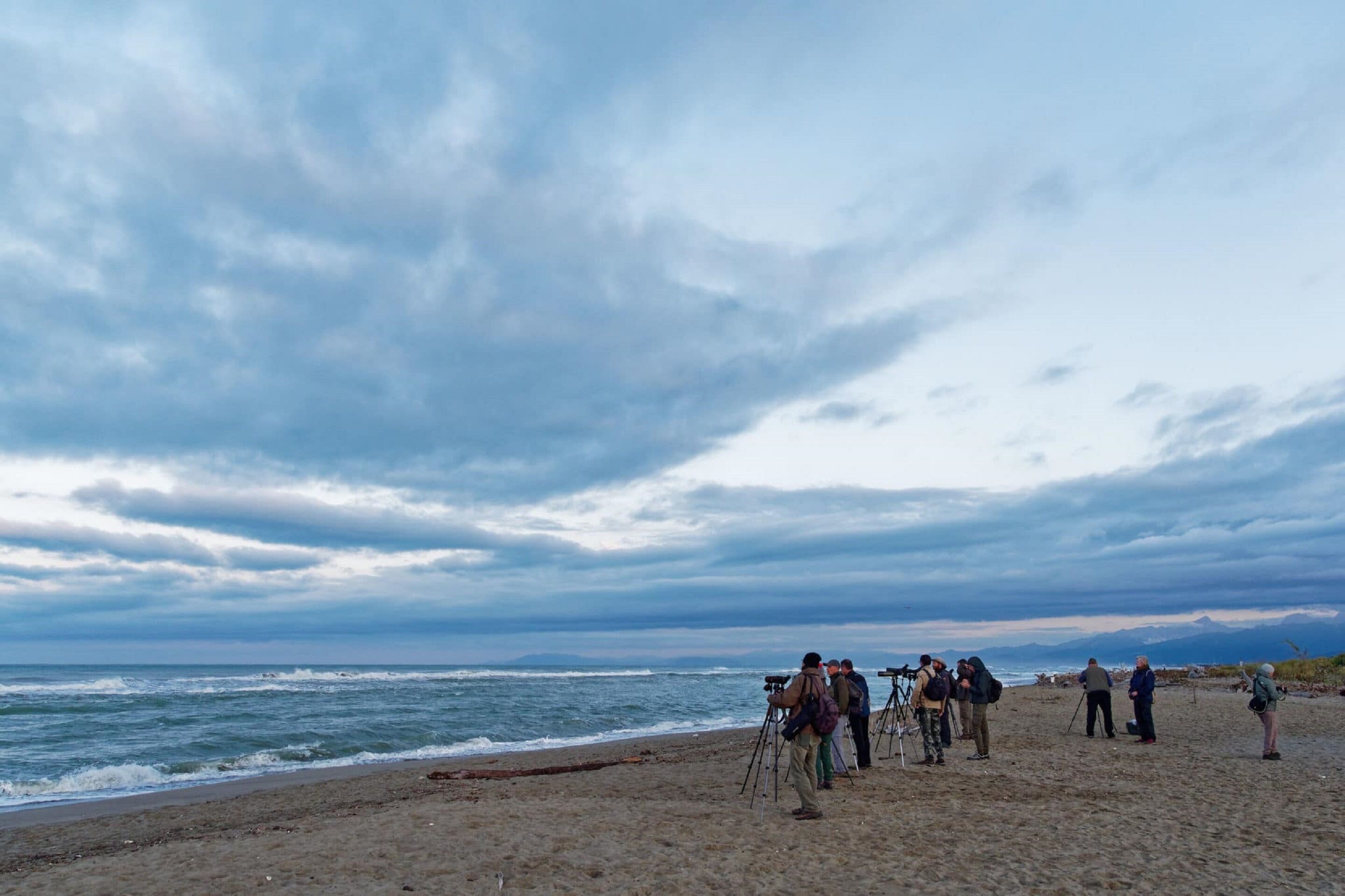 Ein Strand mit Menschen, die Kameras und Stativen benutzen, vermutlich für Fotos oder Dreharbeiten.