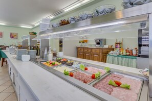 A buffet with various food options, including meats and salads, in a well-lit kitchen area with stainless steel appliances and wooden cabinets. - Hotel Austria (Caorle)