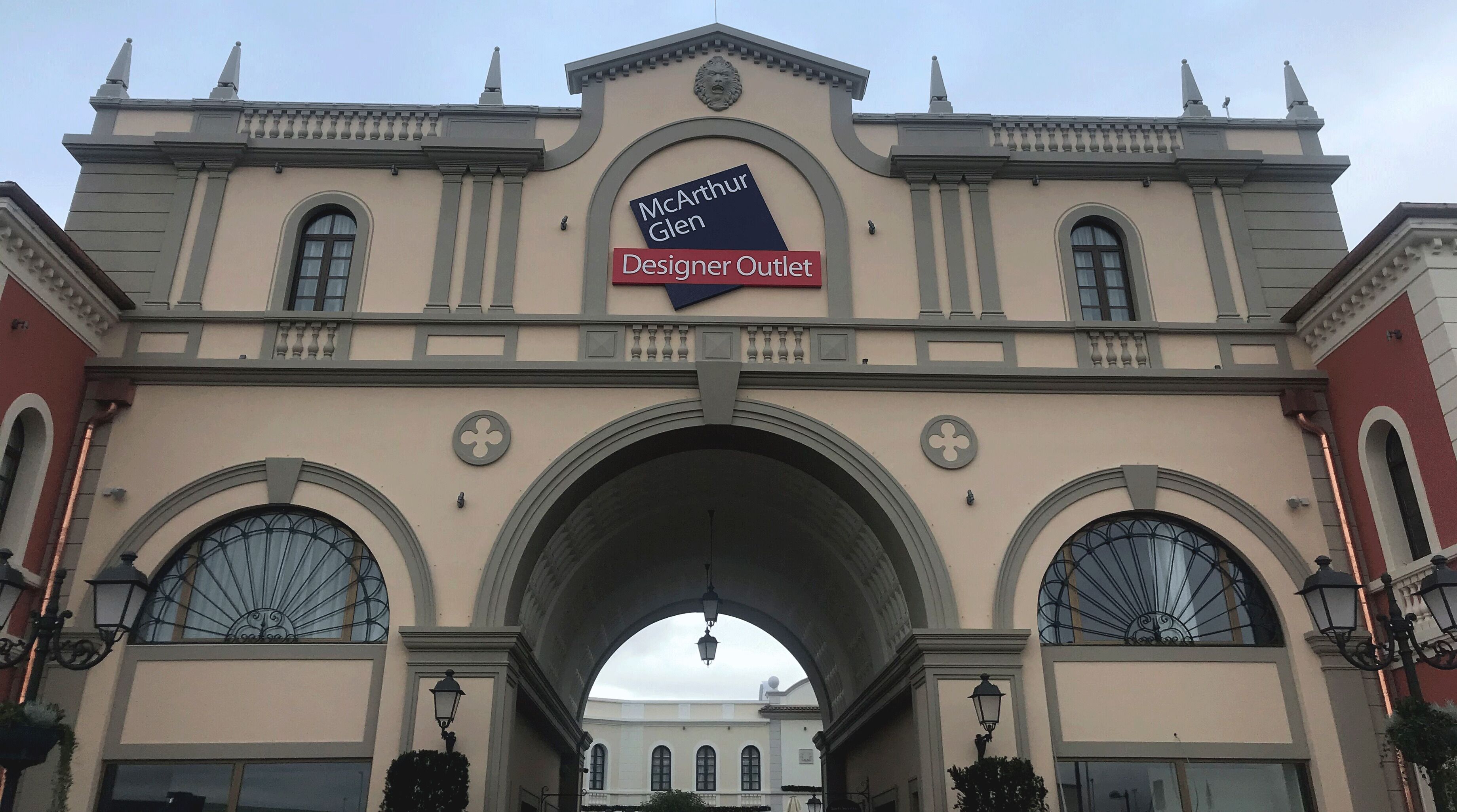 The facade of McArthur Glen Designer Outlet with a central archway and decorative elements.