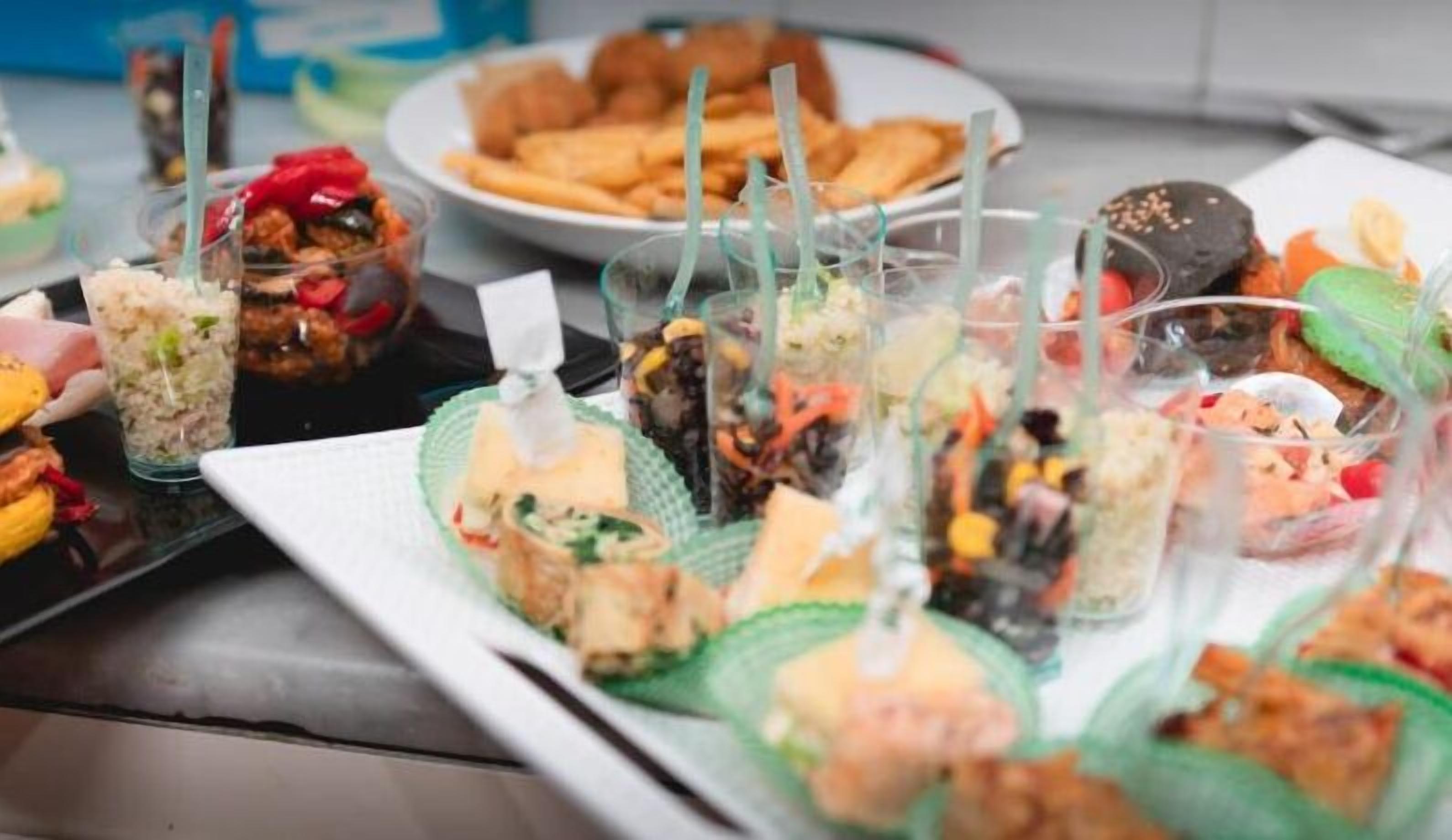 Variedad de alimentos sobre una mesa, incluyendo sándwiches, ensaladas y otros bocadillos.