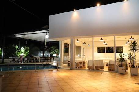 An outdoor dining area with a pool, covered seating, and potted plants.