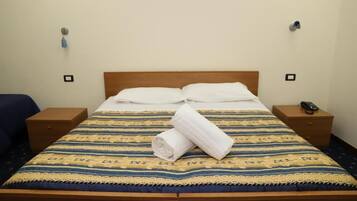 A hotel room with a bed, two bedside tables, a blue chair, and a wooden headboard.