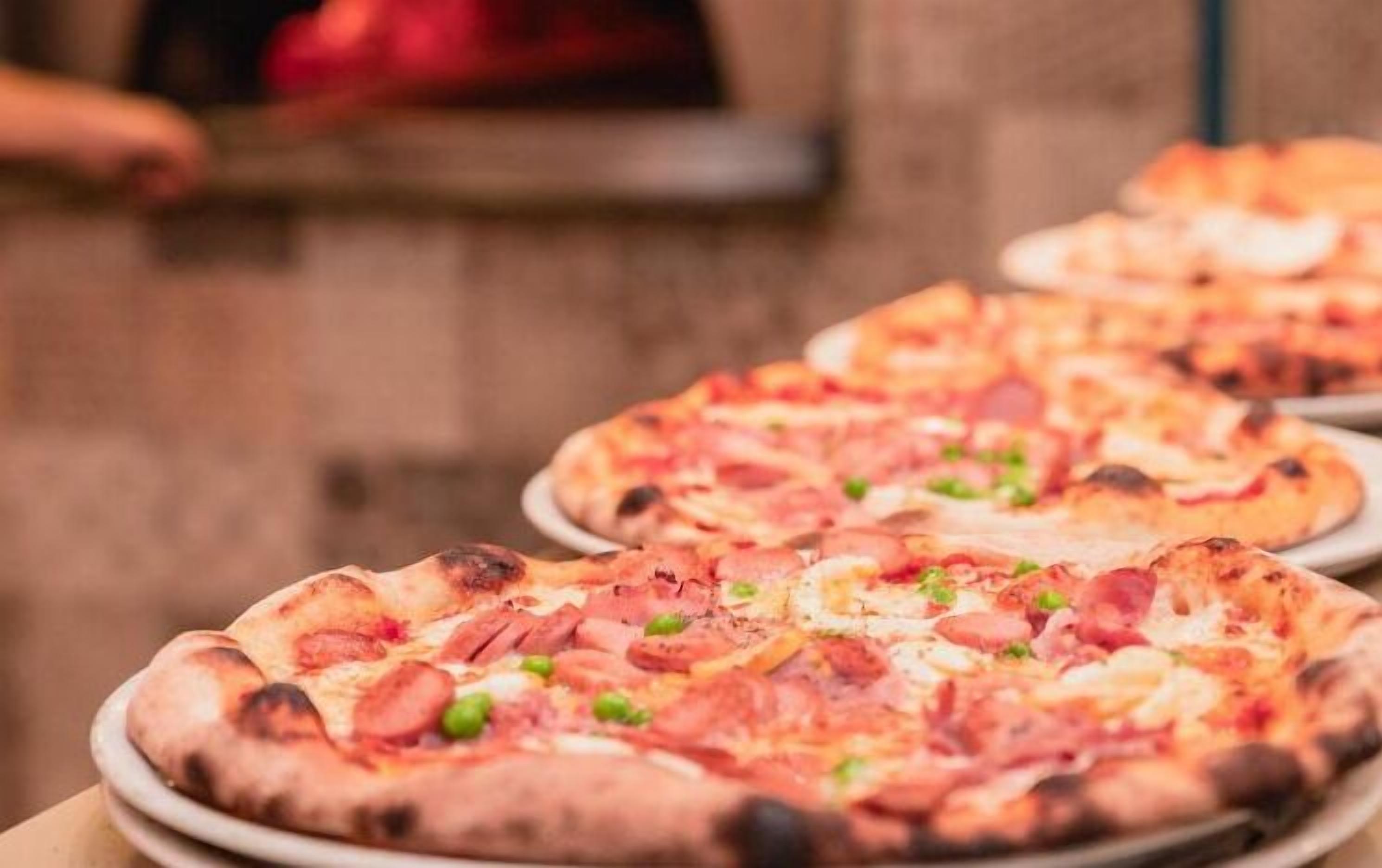 Várias pizzas com pepperoni e pimentões verdes sobre uma mesa.