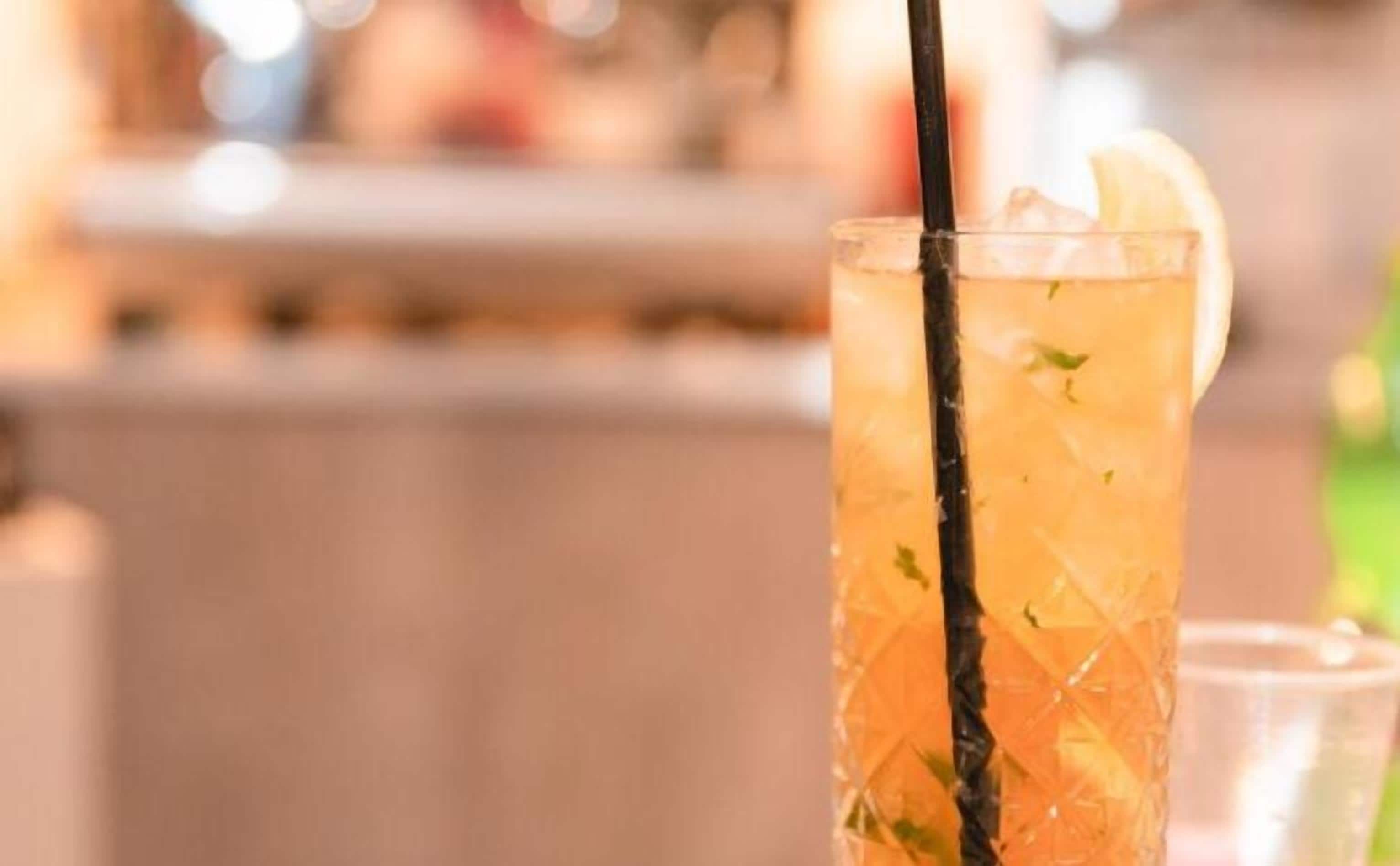 A tall glass with a straw, containing a beverage with ice cubes and a slice of lemon.