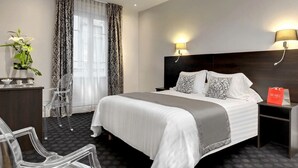 A hotel room with a large bed, two bedside lamps, a desk with a lamp, a chair, and a potted plant. - LOGIS Midland (Vichy)