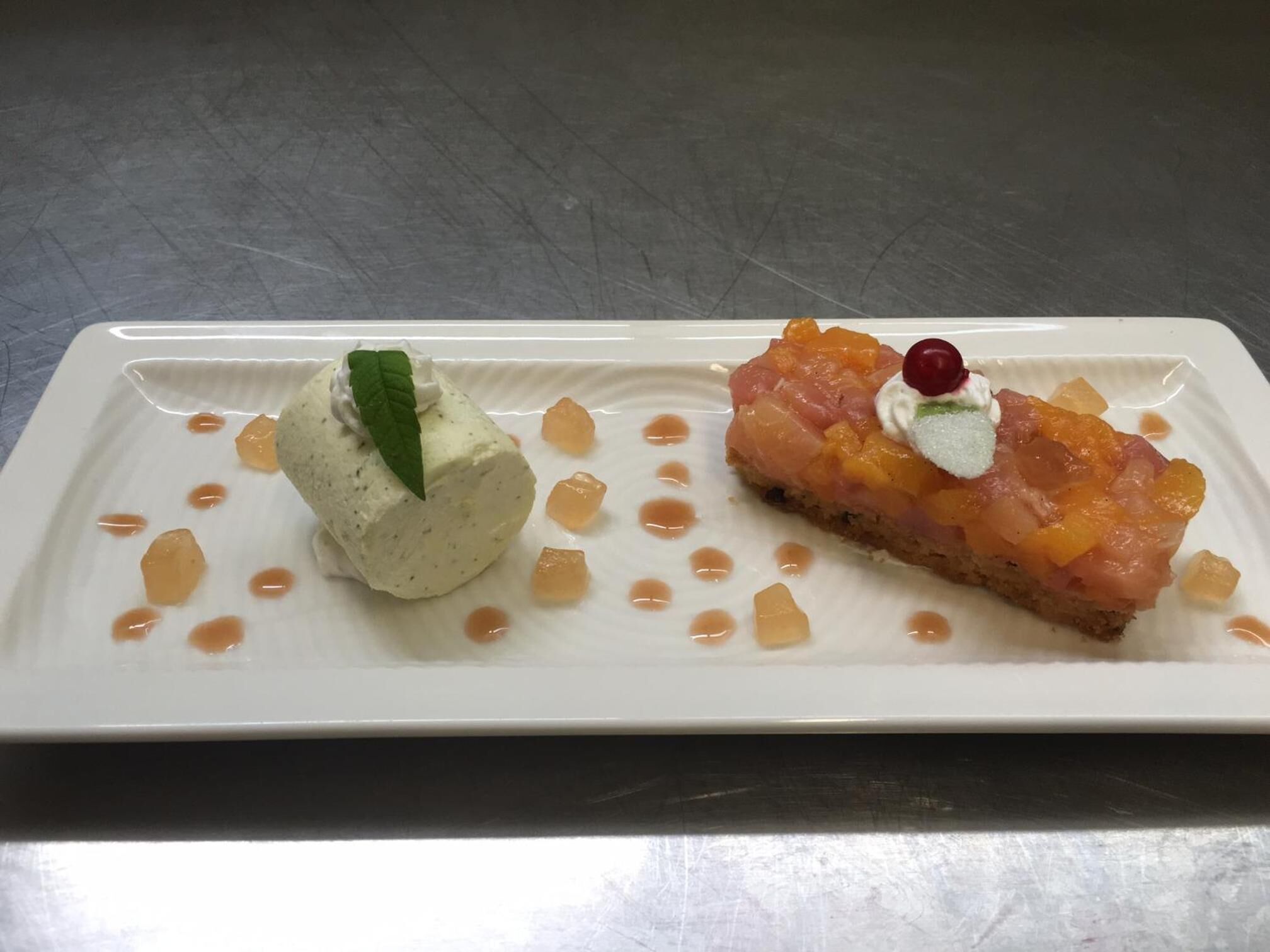 A dessert plate with two different desserts, one with a green leaf garnish and the other with a cherry on top.