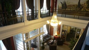 A hotel lobby with a high ceiling, a chandelier, a seating area with sofas and chairs, and a view of the street through large windows. - LOGIS Midland (Vichy)