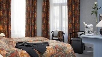 Habitación de hotel con cubrecama floral, un escritorio con lámpara, una silla y una pequeña planta.