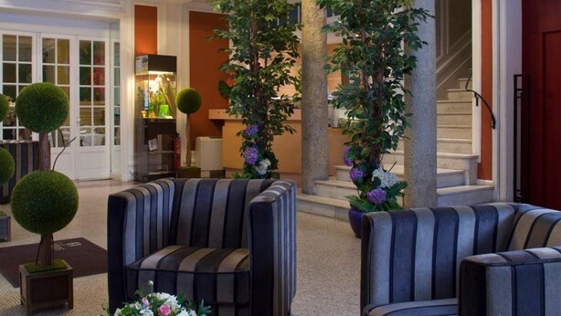 A spacious lobby with a chandelier, seating area, and a staircase. - LOGIS Midland (Vichy)