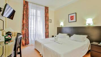Habitación de hotel con dos camas, un escritorio con silla, televisión y ventana con cortinas.