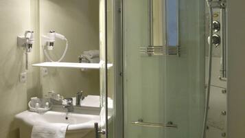 Un baño moderno con ducha de vidrio, tocador con lavamanos y espejo, y un perchero para toallas.