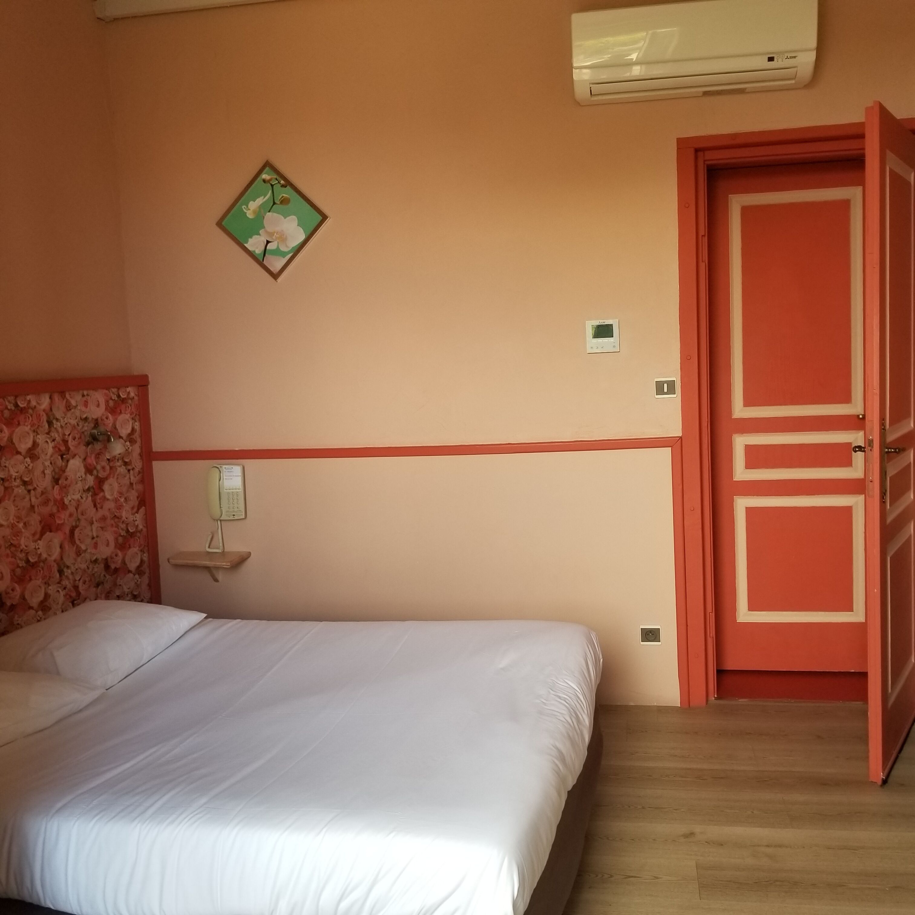 A bedroom with a bed, a wall-mounted air conditioner, a door, and a floral-patterned headboard.
