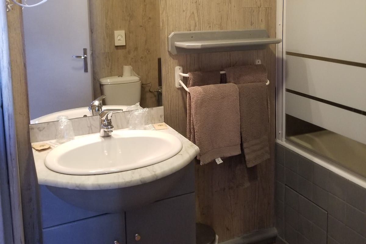 A bathroom with a sink, mirror, toilet, towel rack, and a shower area.