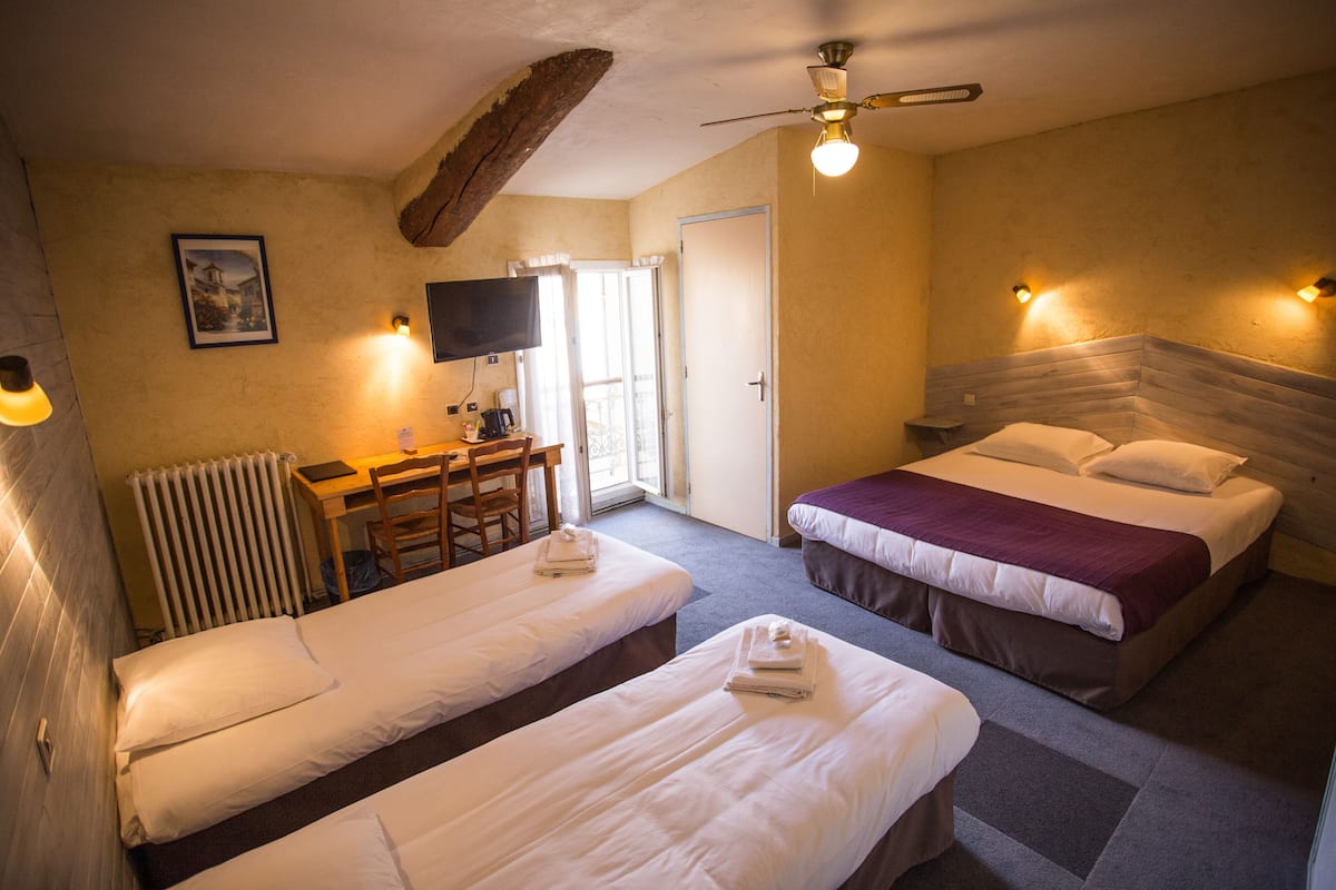 A hotel room with two single beds, a desk with a chair, a television, and a ceiling fan.