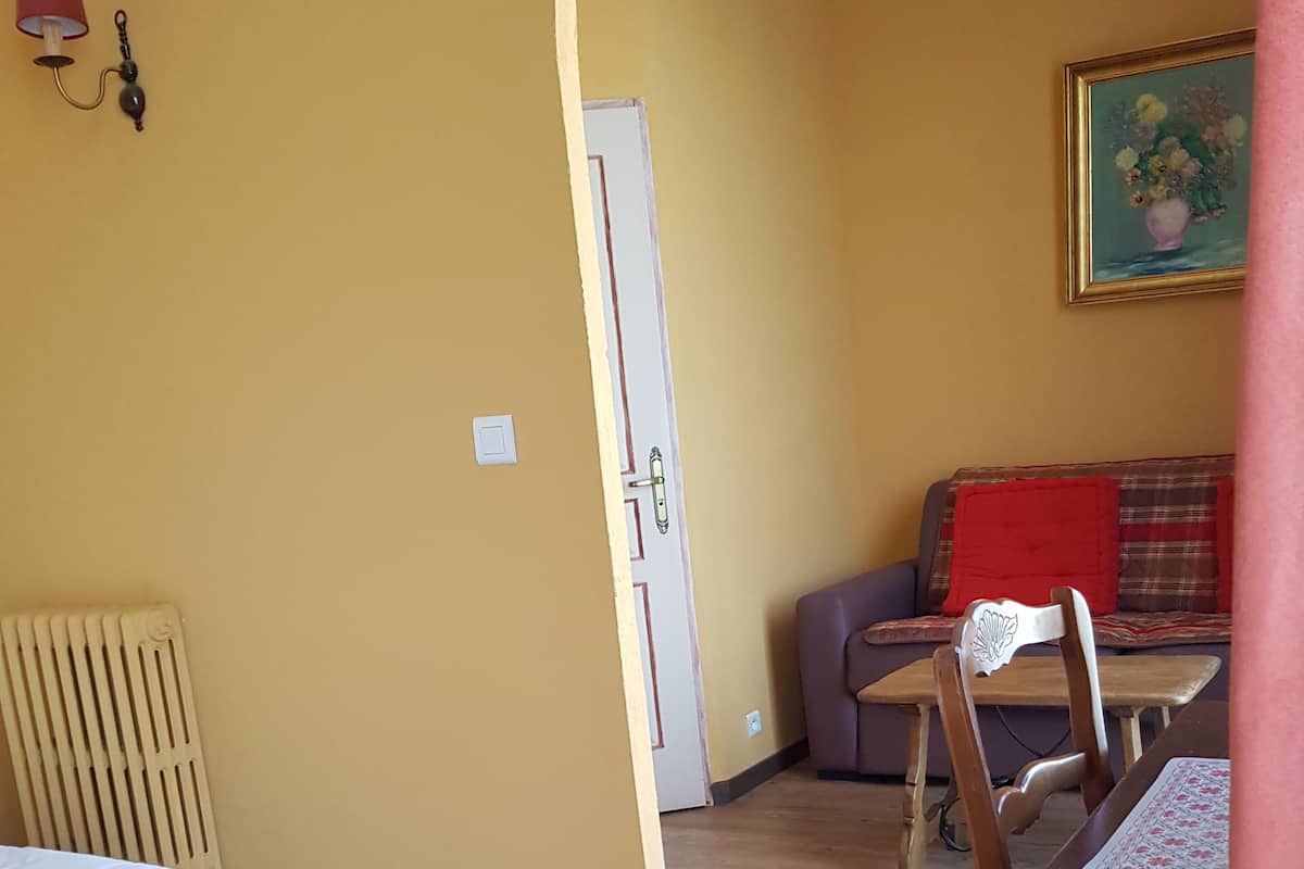 A room with a bed, a wooden floor, a door, a sofa, and a table.