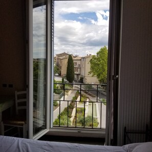 A room with a large window overlooking a street with buildings and greenery. - Logis hôtel du Terreau (Manosque)