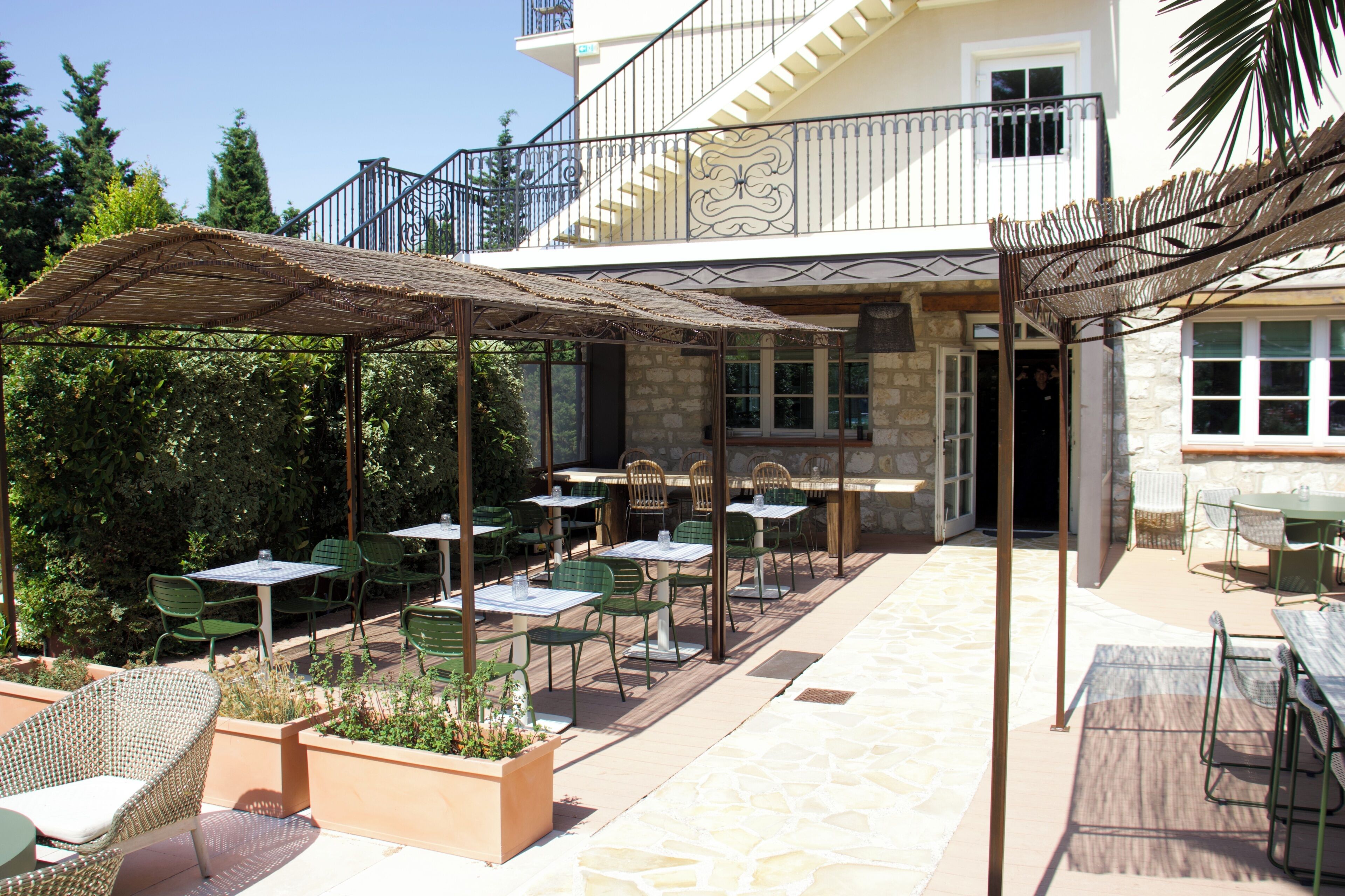 An outdoor patio area with tables and chairs, a covered seating area, and a stone building in the background.