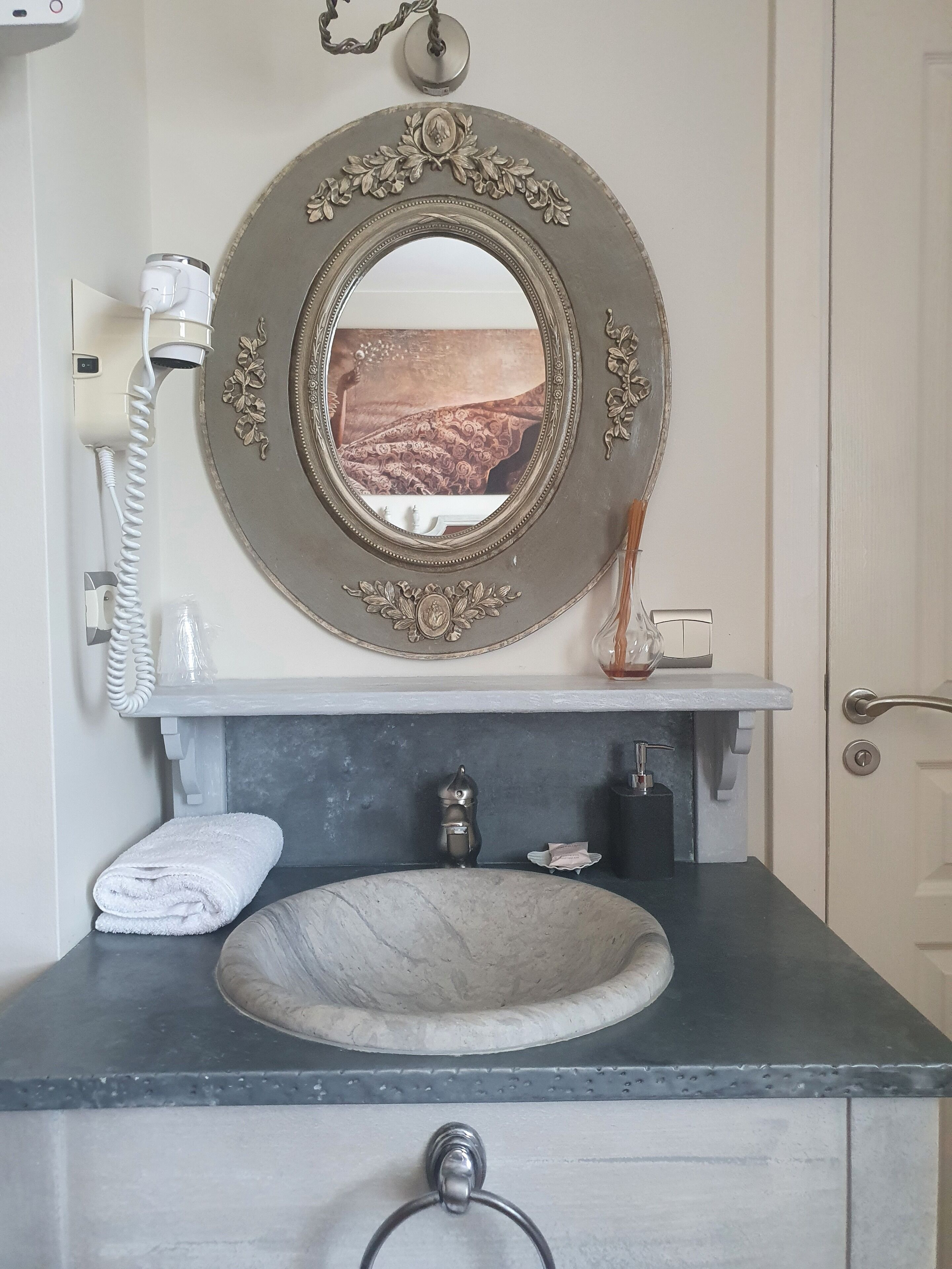 A bathroom with a round mirror, a white towel, a sink, and a showerhead.