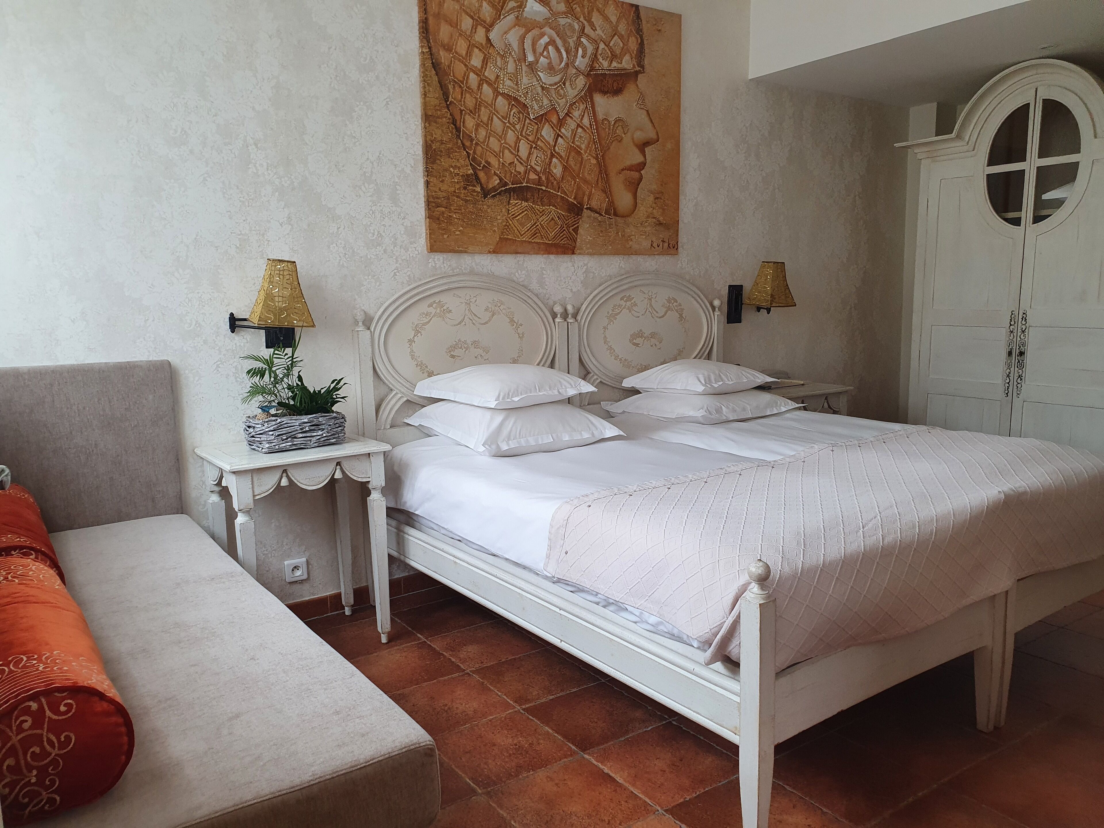 A neatly arranged bedroom with a bed, bedside tables, a lamp, a wardrobe, and a painting on the wall.