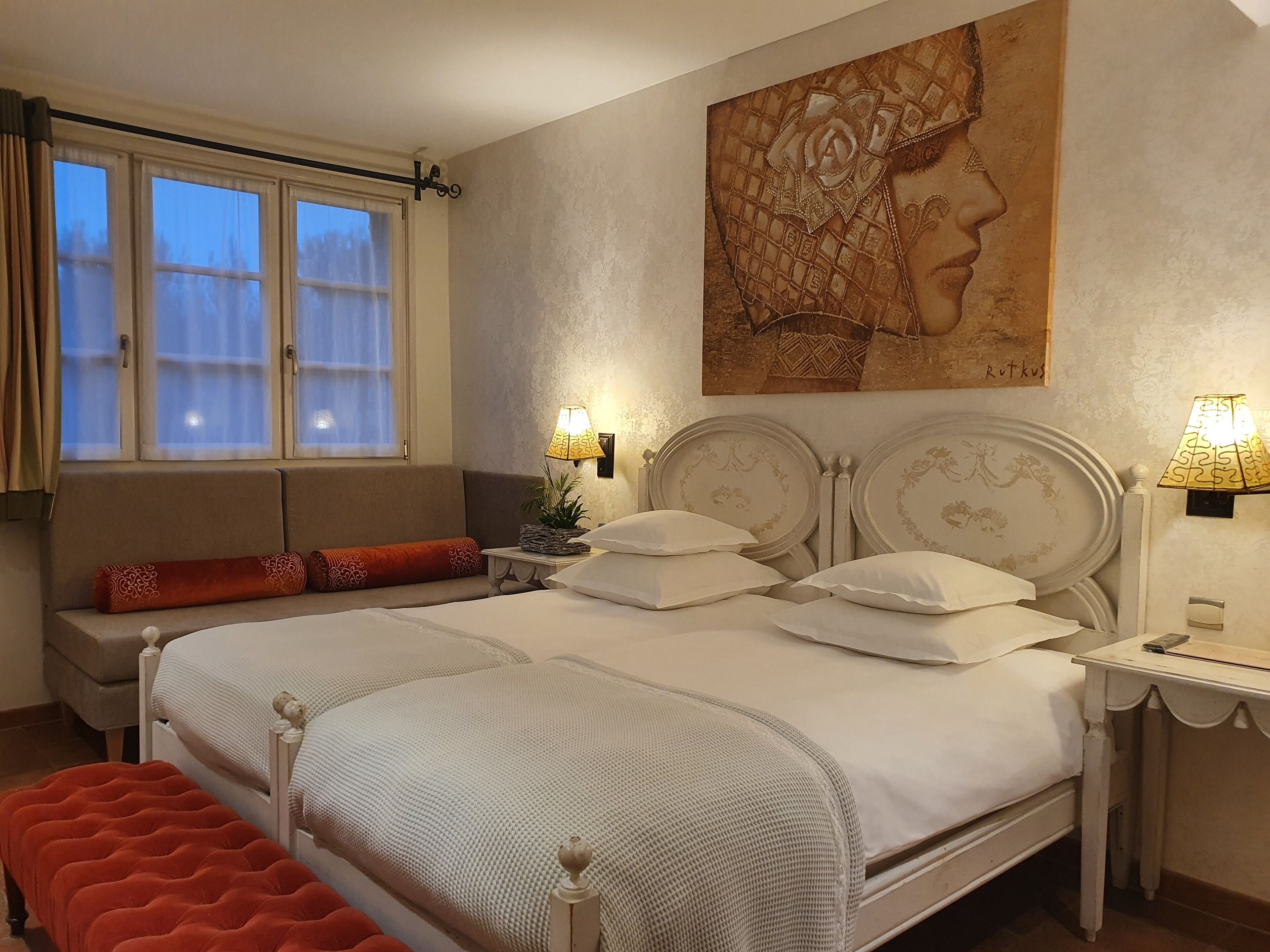 Ein Schlafzimmer mit einem Bett, Nachttischlampen, einem Fenster mit Vorhängen, einem Sofa und einem Bild an der Wand.