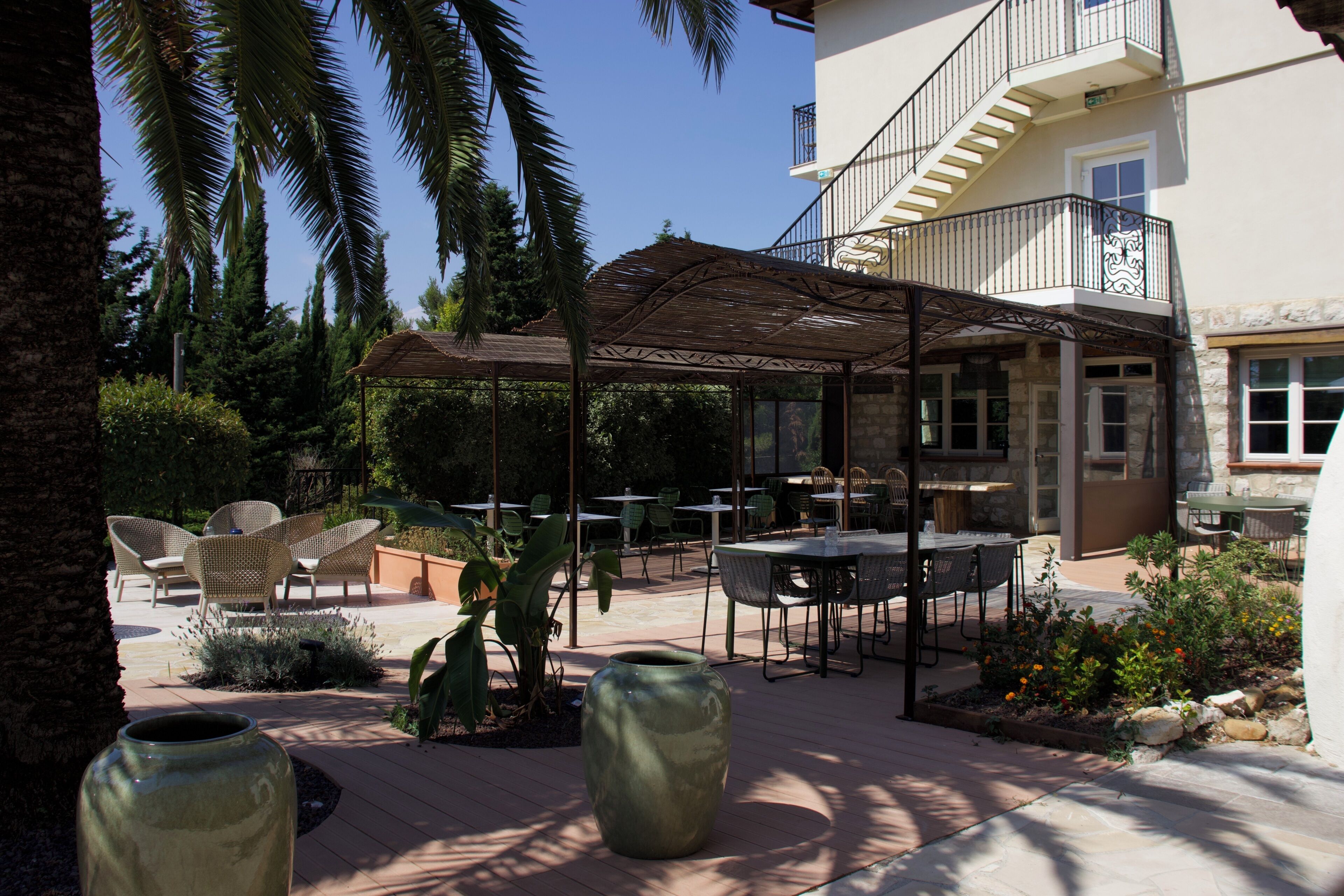 An outdoor patio area with tables and chairs, surrounded by greenery and a covered seating area.