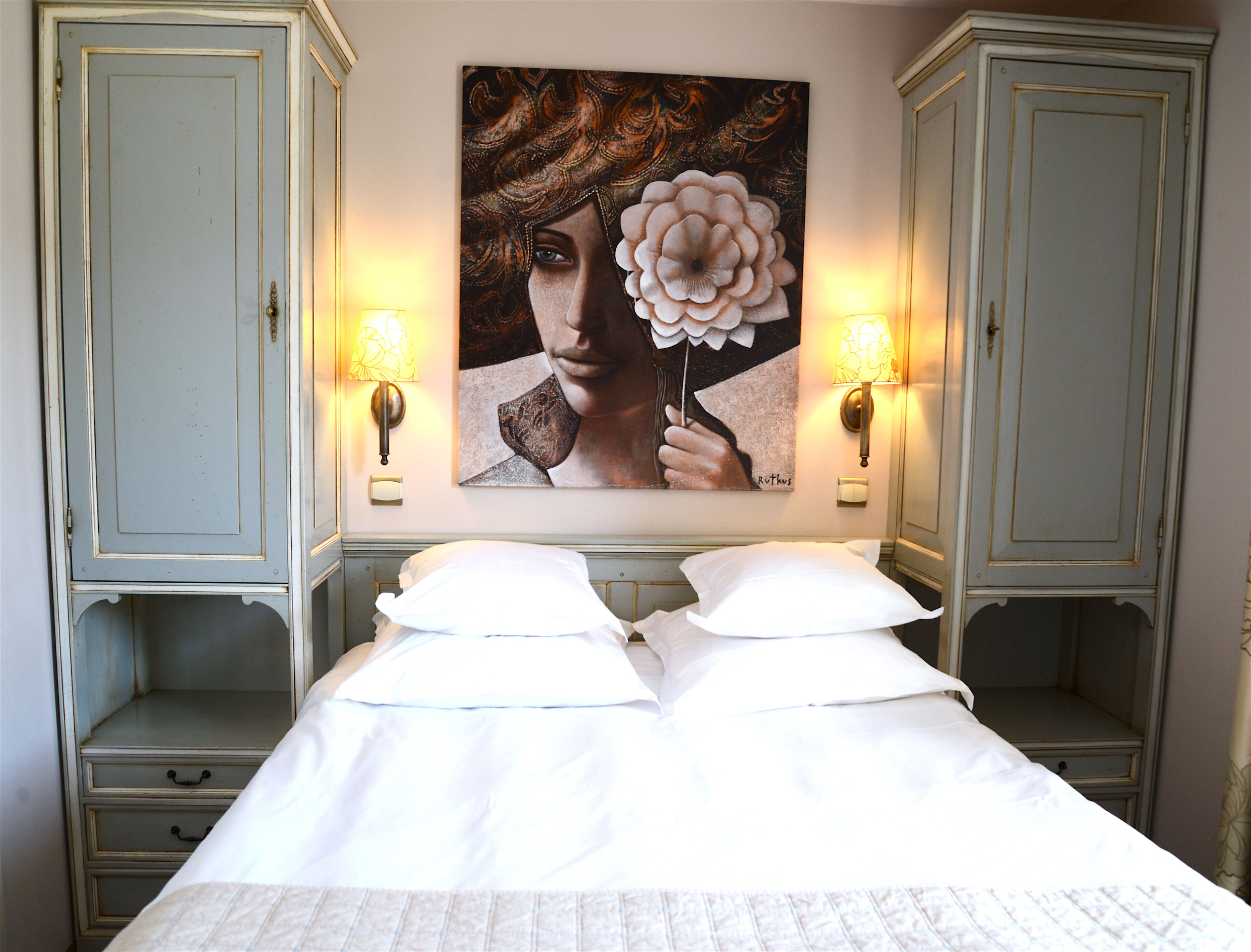 A hotel room with a bed, two nightstands, a wall-mounted painting, and two wall sconces.